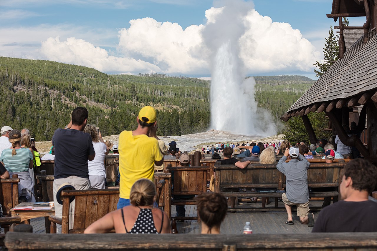 A photograph of people admiring and taking pictures of Old Faithfull erupting